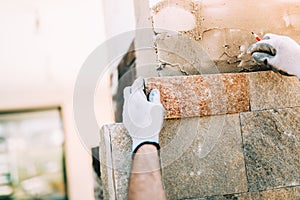 worker with stone tiles in construction site. masonry details on exterior wall with trowel putty knifeworker installing sto