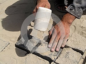 The worker strikes with a white rubber mallet on granite pavement stones