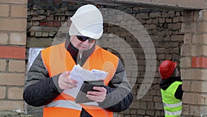 Worker with tablet PC and documentation near building