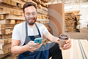 Worker taking a break and looking at mobile at storehouse