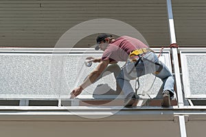 A worker taping a balcony for painting. The painter hangs from safety ropes and straps.