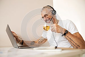 Worker with tattooed arms drinking tea and touching the screen