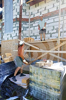 A worker throws bricks at another worker, construction work in a private area, wooden scaffolding near the walls