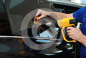 Worker tinting car window with heat gun in workshop, closeup