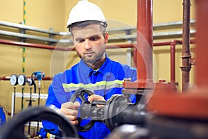 Worker turning gate valve on boiler pipe