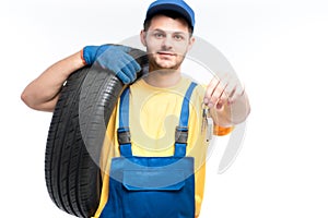 Worker in uniform holds tire and car keys in hands