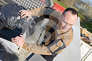 Worker unloading rubbish bags at tip