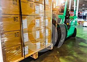 Worker unloading shipment carton boxes and goods on wooden pallet by forklift  from container truck to warehouse cargo storage in