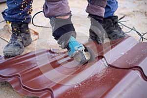 Worker use grinding machine for cutting metal roof sheets. A roofer uses an electric tool when building a house