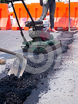 Worker use vibratory plate compactor compacting asphalt at road