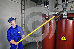 Worker uses insulating rod to earth grounding transformer. photo