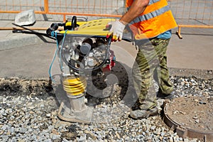 A worker uses a portable vibration rammer during road repairs.