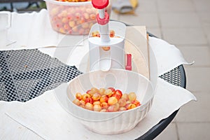 Worker uses a simple tool to extract pits from fresh cherries and prepare them for further use. Manual work with fruit. Seasonal