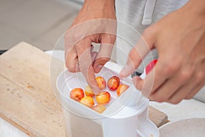 Worker uses a simple tool to extract pits from fresh cherries and prepare them for further use. Manual work with fruit. Seasonal