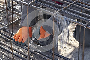 A worker uses steel tying wire to fasten steel rods to reinforcement bars. Close-up. Reinforced concrete structures - knitting of