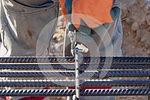 A worker uses steel tying wire to fasten steel rods to reinforcement bars. Close-up. Reinforced concrete structures - knitting of