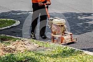 Worker uses vibratory plate compactor compacting asphalt at road repair