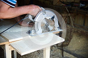 A worker using a circular saw works with wood in a carpenter`s workshop