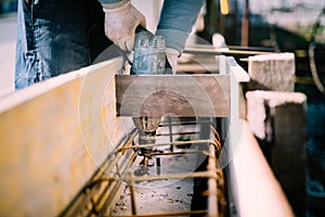 Worker using a drill power tool on construction site and creating holes in cement for foundation reinforcement