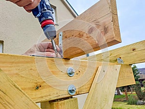 Worker using drill working on construction of wood frame house, gazebo