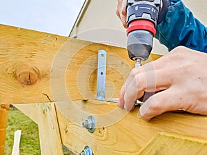 Worker using drill working on construction of wood frame house, gazebo