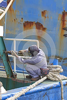 Worker using electric steel cracker to polishing the old rusty stern ladder of oil tanker at dockyard in vertical frame