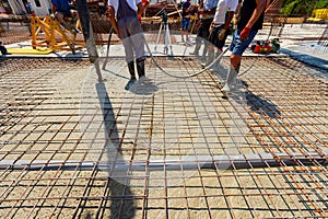 Worker is using electric vibratory to compact concrete in foundation among reinforcing steel bars
