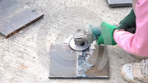 Worker using electric wheel grinding disc grinds metal plate in workplace.