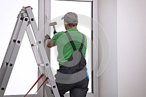Worker using hammer for double glazing window installation indoors, back view