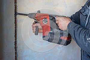 Worker using a jackhammer to drill into wall for electricity installation, on construction site