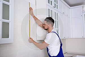 Worker using measuring tape while installing furniture in kitchen