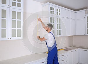 Worker using measuring tape while installing new furniture in kitchen