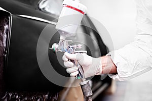 Worker using a paint spray gun for painting a car