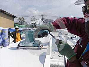 Worker is using a Ponceuse Vibrante or Orbital Sander to scrub surface intermediate fire proof paint before painting top coat photo