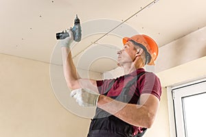 Worker is using screws and a screwdriver to attach plasterboard to the ceiling
