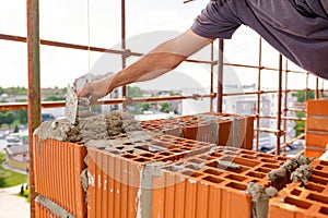 Builder using spatula to set up mortar over red brick, building site