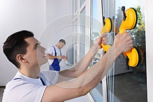 Worker using suction lifters during plastic window installation indoors photo