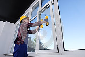 Worker using suction lifters during plastic window installation indoors photo