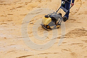 Worker using vibratory plate compactor for compaction sand during path construction.