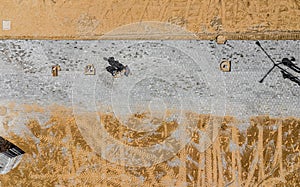 Worker with vibratory plate compactor compacting sand at road or sidewalk construction site top view