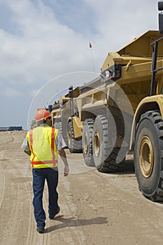 Worker Walking Near Trucks At Landfill Site