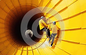 A worker walks on a ladder under a large pipe on an oil rig in the middle of the sea