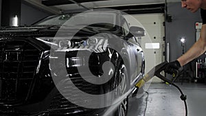 The worker washes the black of a SUV with a high pressure washer at a car wash.