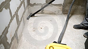 Worker washes the floor with a vacuum cleaner from industrial concrete dust and cement mud during home renovation. A