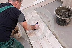 The worker washes freshly laid tiles on the bathroom floor with cement glue