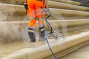 worker washes the pavement. Worker in uniform washes street with street washing machine. Municipal service of city