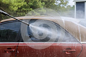 Worker washing his car under a high pressure jet spraying water along with cleaning his car