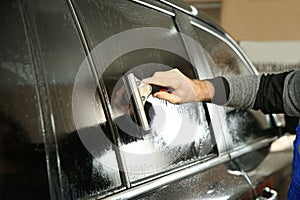 Worker washing tinted car window in shop