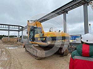 Worker watching digger moving waste at landfill site