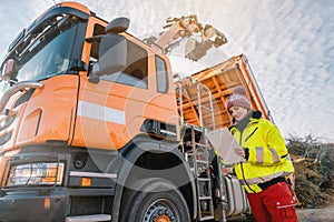 Worker watching a lorry with gripper unloading biomass